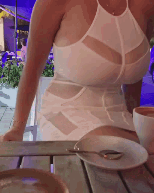 a woman in a white dress sits at a table with a cup of coffee and a plate of food