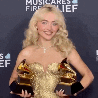a woman in a gold dress is holding two grammys in her hands .