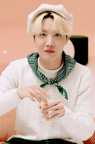 a young man wearing a white sweater and a green scarf around his neck looks at something