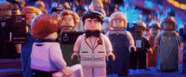 a group of lego figures are standing in a room with a woman holding a piece of paper .