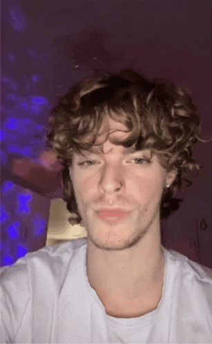 a young man with curly hair is wearing a white shirt and a nose ring
