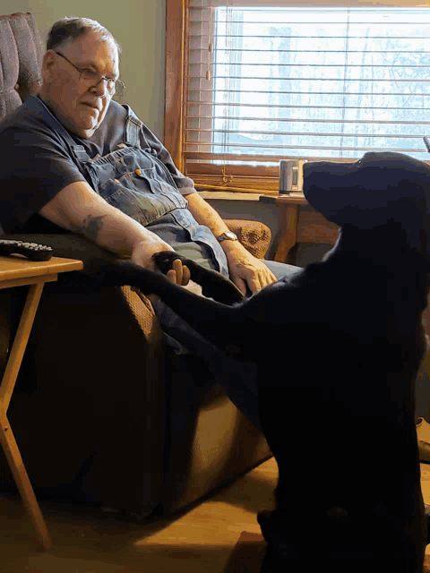 a man sitting in a chair with a black dog standing next to him