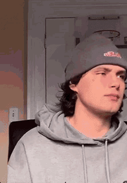 a young man wearing a gray hoodie and a purple beanie .