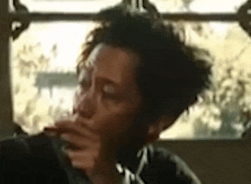 a man is smoking a cigarette in front of a window while sitting in front of a window .
