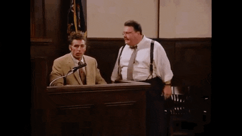 two men are standing in front of a podium in a courtroom talking into microphones .