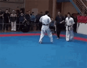 two karate fighters are fighting on a blue mat with a crowd watching