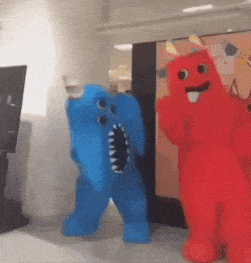 a blue elephant costume and a red monster costume are dancing together in a room .