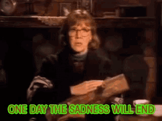 a woman is sitting at a table with the words " one day the sadness will end "