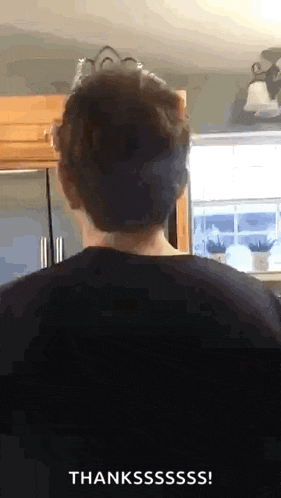 a man in a black shirt is standing in front of a window in a kitchen and says thanksssss .