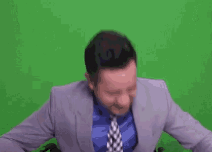 a man in a suit and tie is sitting in front of a green screen and making a funny face .