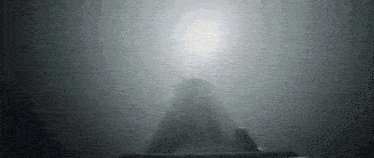 a black and white photo of a mountain with a light behind it