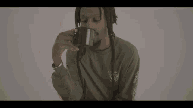 a man in a green shirt is drinking from a black mug .