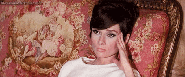 a woman laying on a couch with her hand on her forehead and a floral rug behind her