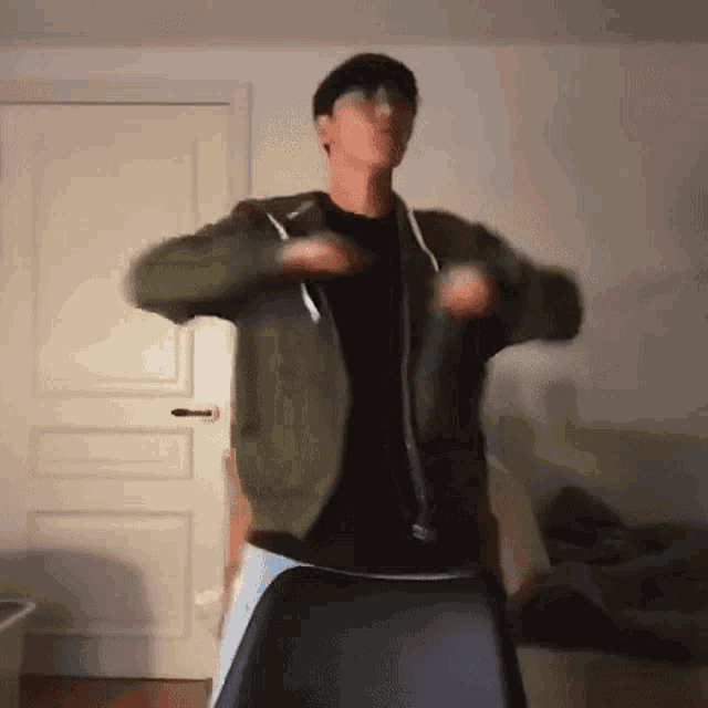 a man in a green jacket and black shirt is dancing in a room .