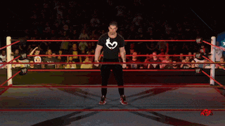 a man in a black shirt with a heart on it is standing in a ring