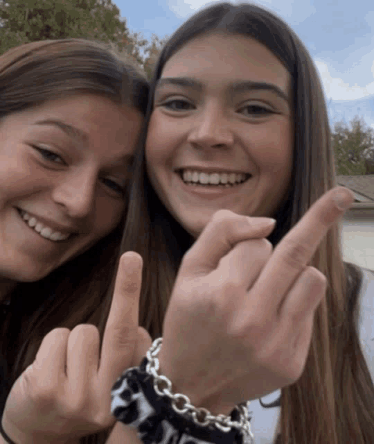 two girls are giving the middle finger and one has a bracelet that says chanel