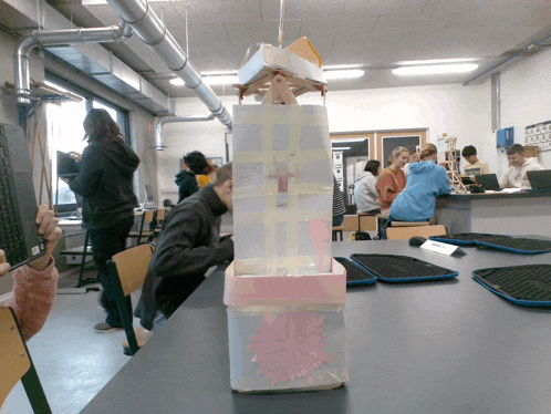 a group of people are sitting at a table with a tower made out of cardboard and tape
