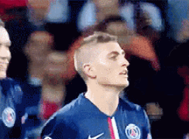 a soccer player wearing a nike jersey stands in front of a crowd of people .