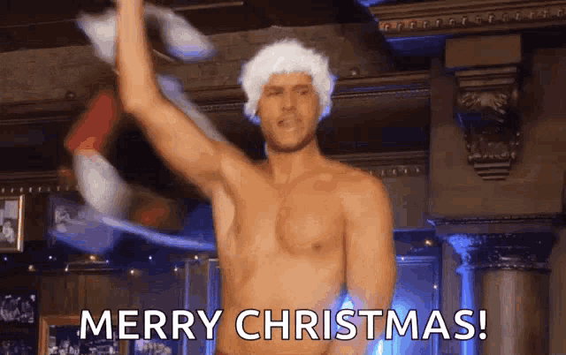 a shirtless man is wearing a santa hat and dancing in a room .