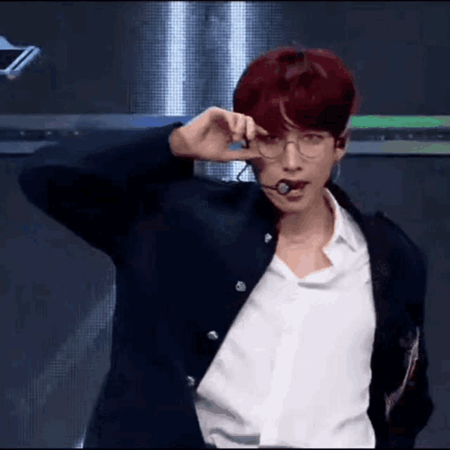 a man with red hair is wearing glasses and a microphone while standing on a stage .