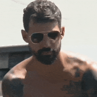 a shirtless man with a beard and sunglasses is standing in front of a car .