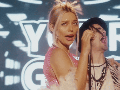 a woman in a pink dress sings into a microphone in front of a sign that says y-g-r