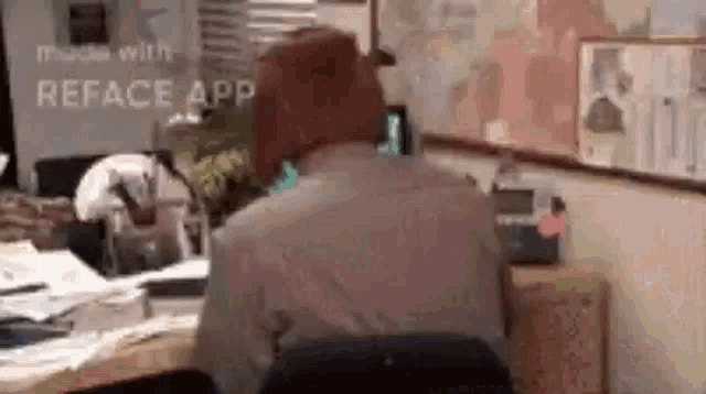 a man is sitting at a desk in front of a computer in an office with his back to the camera .