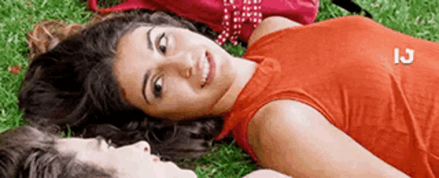 a man and a woman are laying in the grass and the woman is wearing a red tank top