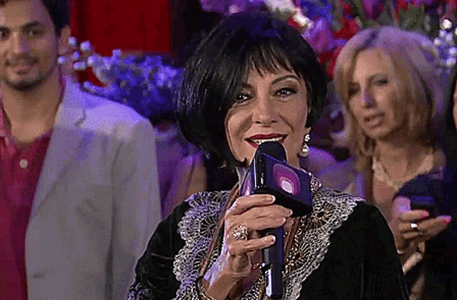 a woman is smiling while holding a microphone in front of a crowd of people