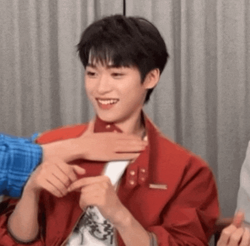 a young man in a red jacket is being touched by someone .