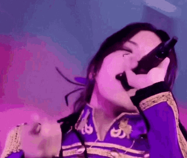 a woman is singing into a microphone while wearing a purple outfit .