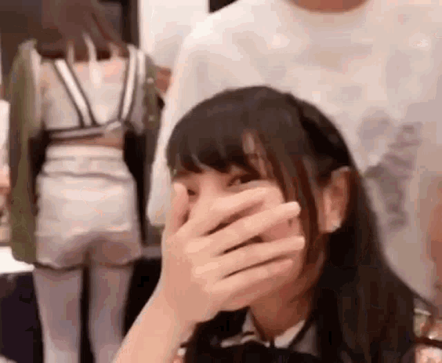 a girl is covering her face with her hand while a man stands behind her .