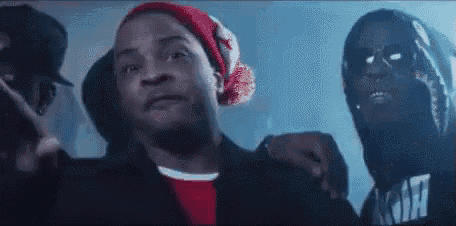 a group of men are standing next to each other in a dark room . one of the men is wearing a red beanie .