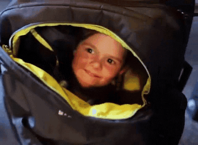 a little girl is smiling while looking out of a black bag .