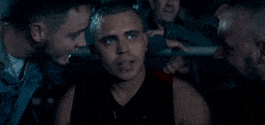 a man is drinking from a plastic bottle while another man looks on