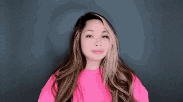 a woman wearing a pink sweater is waving her hand