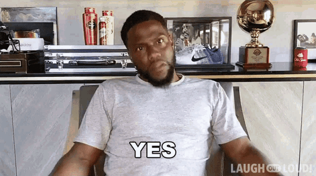 a man in a grey shirt says yes while sitting in front of trophies
