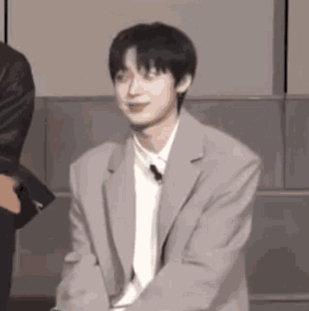a young man in a suit is sitting on a chair and smiling .