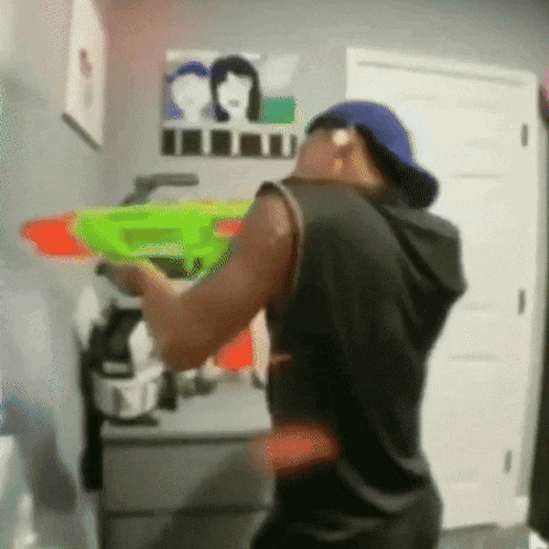 a man in a black tank top and blue hat is holding a green water gun