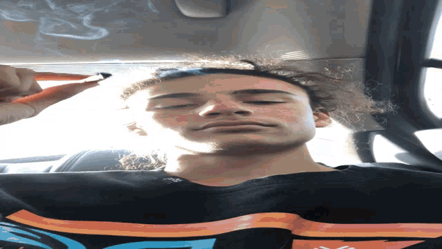 a man smoking a cigarette in a car wearing a black shirt with a rainbow design