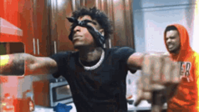 a man wearing a bandana on his eyes is standing in a kitchen .