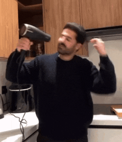 a man in a black sweater is blow drying his hair .