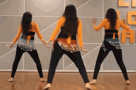 three women are dancing in front of a wall with the letter a behind them