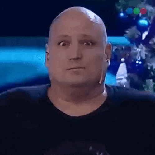 a bald man wearing a black shirt and ear buds looks at the camera