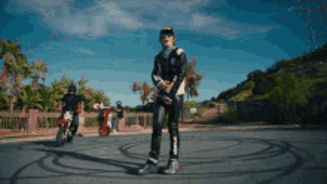a man in a black leather jacket is standing in a circle with two motorcycles behind him