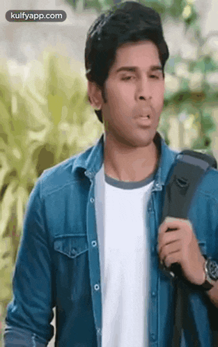 a young man wearing a denim jacket and a white shirt is holding a backpack .
