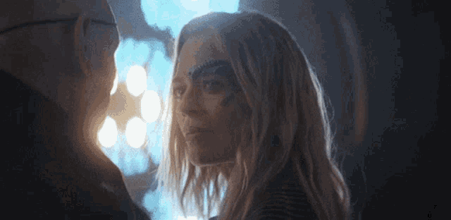 a man and a woman are looking at each other in a dark room . the woman has a mask on her face .