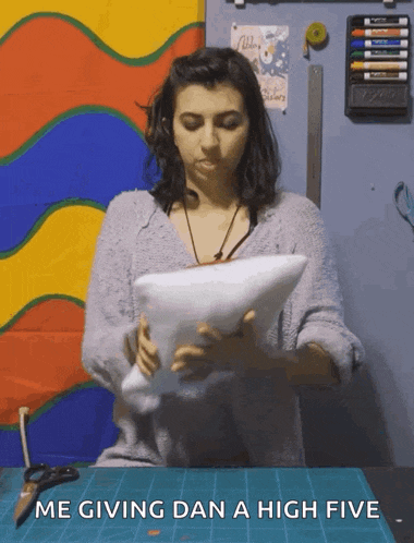 a woman holding a pillow with the words me giving dan a high five