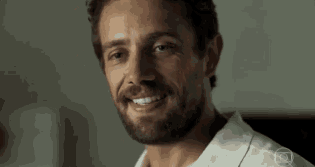 a man with a beard is smiling for the camera while wearing a white shirt .