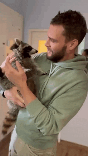 a man in a green hoodie holds a raccoon in his arms